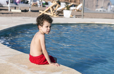 Curly-haired boy sitting at the edge of the pool