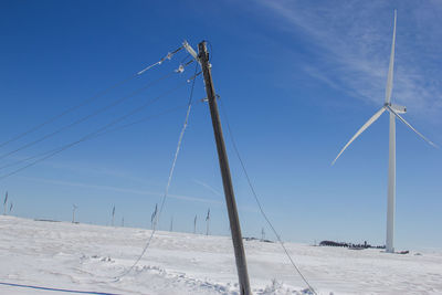 Leaning power pole with wind turbines in the background.