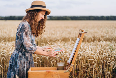 Side view of woman wearing hat standing on field