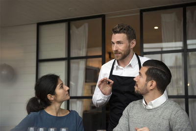 Smiling man discussing with business people while gesturing during winetasting