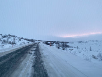 Snow covered road amidst snowcapped landscape against sky