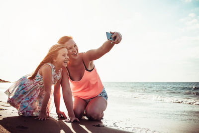 Cheerful mother and daughter taking selfie at beach