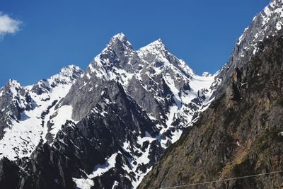 Low angle view of snowcapped mountains against clear blue sky