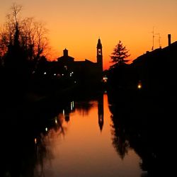 Reflection of silhouette trees and buildings on lake during sunset