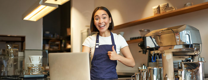 Portrait of young woman using mobile phone while standing in cafe