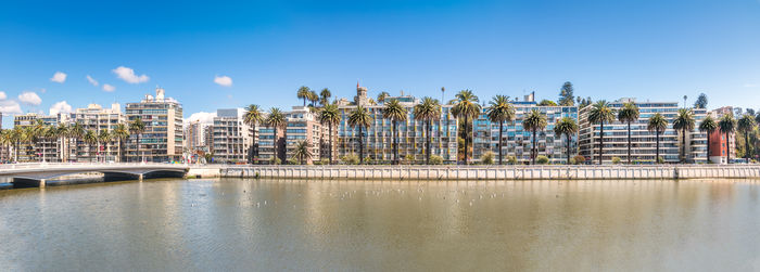 Buildings by river against clear blue sky