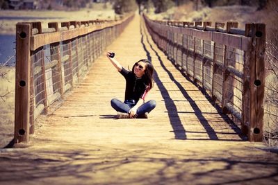 Full length of girl taking selfie while sitting on footpath