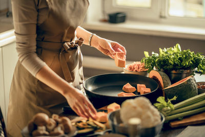 Hands of young woman put pumpkin on frying pan for baking in kitchen. the concept of healthy eating