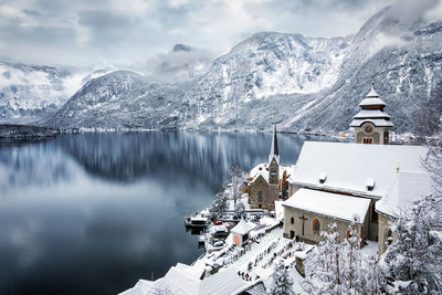 Snow covered buildings by lake during winter