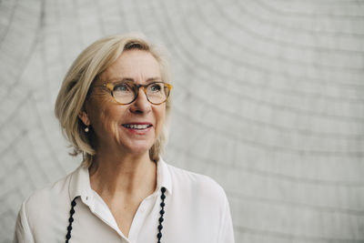 Thoughtful smiling senior businesswoman against wall in office