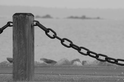 Close-up of chain on wooden post at beach