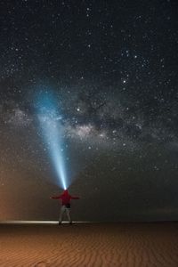 Man with illuminated headlamp standing at beach against star field