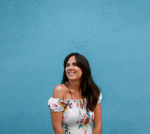 Portrait of a happy beautiful young woman in white dress against blue wall background.