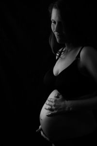 Smiling pregnant woman looking away while standing in darkroom