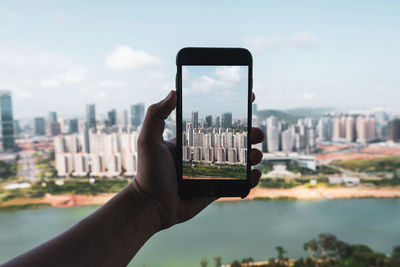 Midsection of man holding mobile phone against buildings in city