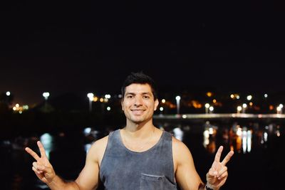 Portrait of smiling man standing against illuminated city at night