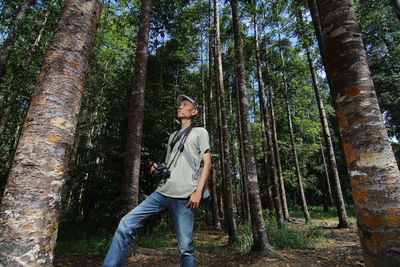 Young man standing by tree trunk in forest