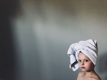 Portrait of cute girl with head wrapped in towel against wall