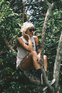 Full length of woman looking away while sitting on tree