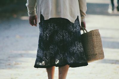 Rear view of woman carrying wicker shopping bag on footpath