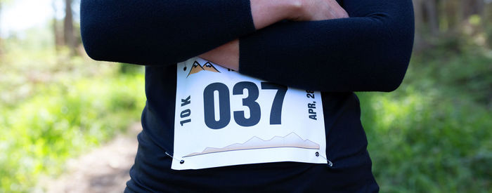 Midsection of woman standing with marathon bib in forest