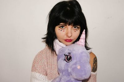 Portrait of mature woman holding stuffed toy while standing against wall