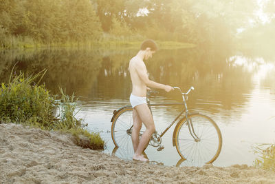 Side view of man in underwear standing with bicycle at lake