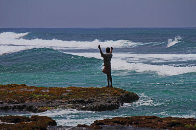 Man standing on rock at beach against sky