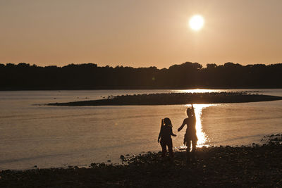 Silhouette people on beach against sky during sunset