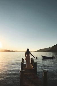 Rear view of woman standing on pier by sea against clear sky