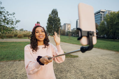 Woman waving hand while vlogging through smart phone at park