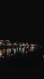 Illuminated city by sea against clear sky at night