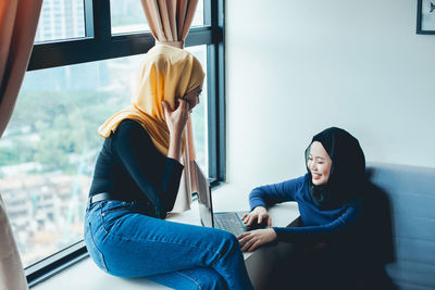 Young woman sitting on window at home