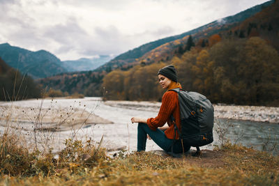 Side view of man sitting on mountain against sky