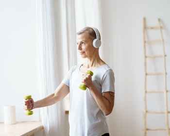 Active senior woman exercising fitness with dumbbells, build up biceps, train arms triceps.