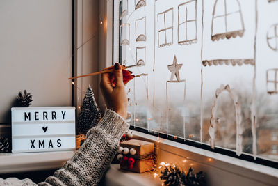 Female hand draws christmas holidays decoration painted on window glass. 