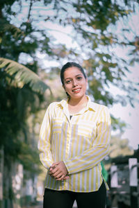 Portrait of smiling young woman standing against trees