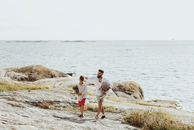 Father with blanket walking by son against sea during summer