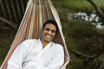 Smiling young man in bathrobe relaxing in hammock