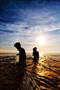 Silhouette fishermen fishing in sea against sky during sunset