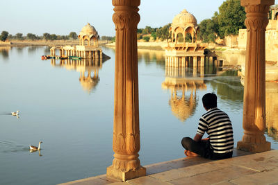 Rear view of man sitting in gazebo on lake