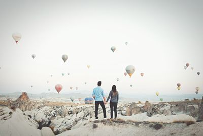 Rear view of people watching balloons on rocks against sky