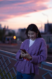 Portrait of smiling young woman standing against sky during sunset