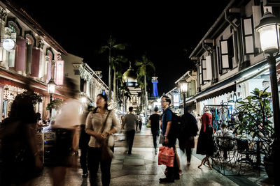 People walking on illuminated street in city at night