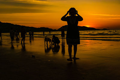 Silhouette woman walking on beach against orange sky