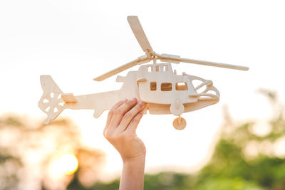 Cropped hand holding wooden toy helicopter against sky