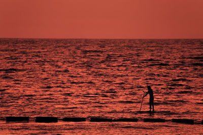 Silhouette woman paddleboarding on sea during sunset