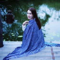 Portrait of woman wrapped in blanket sitting on jetty over lake