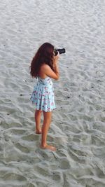 High angle view of young woman photographing through camera while standing at beach