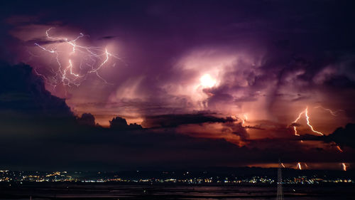 Lightning over illuminated cityscape against dramatic sky at night